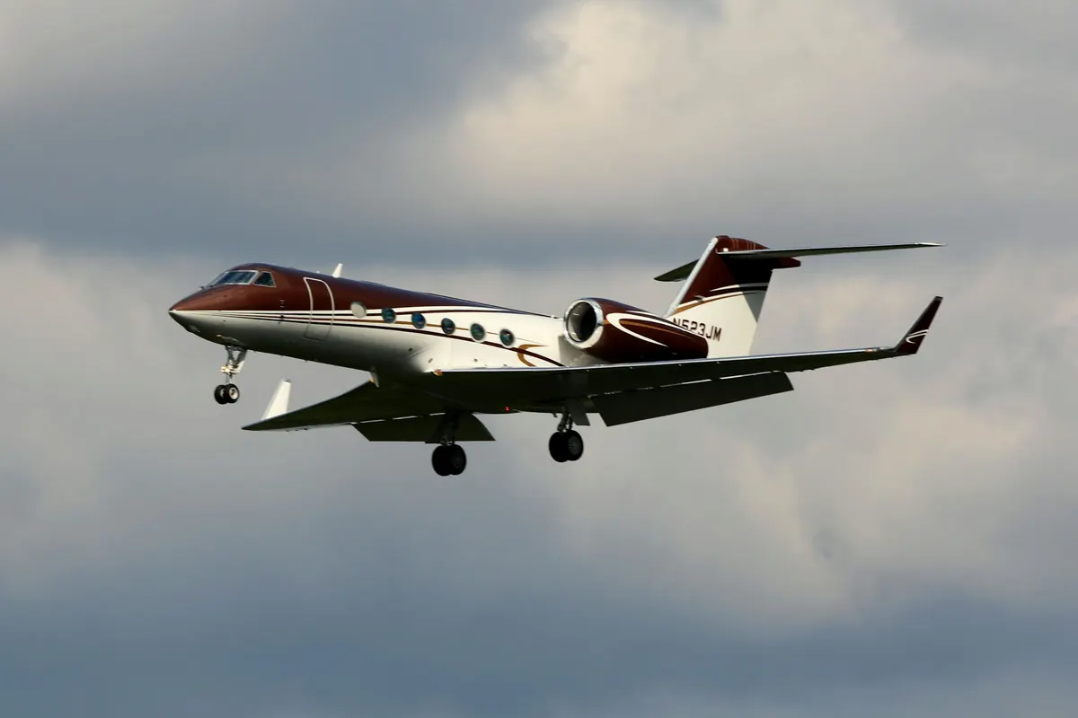 Light business jet in flight with its landing gear down against grey cloud