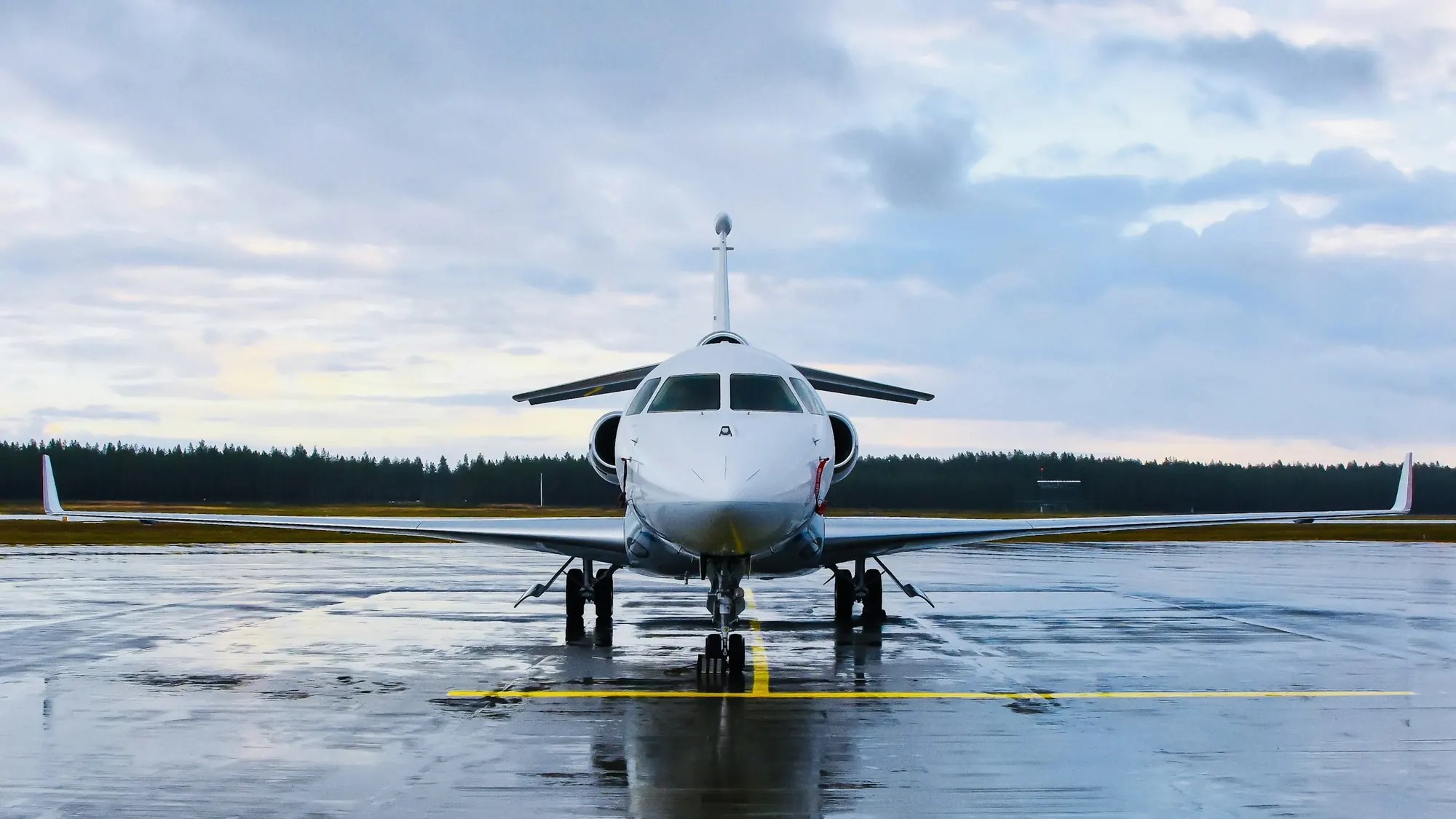 Business jet seen nose-on, parked on a rain-wet ramp under grey cloud
